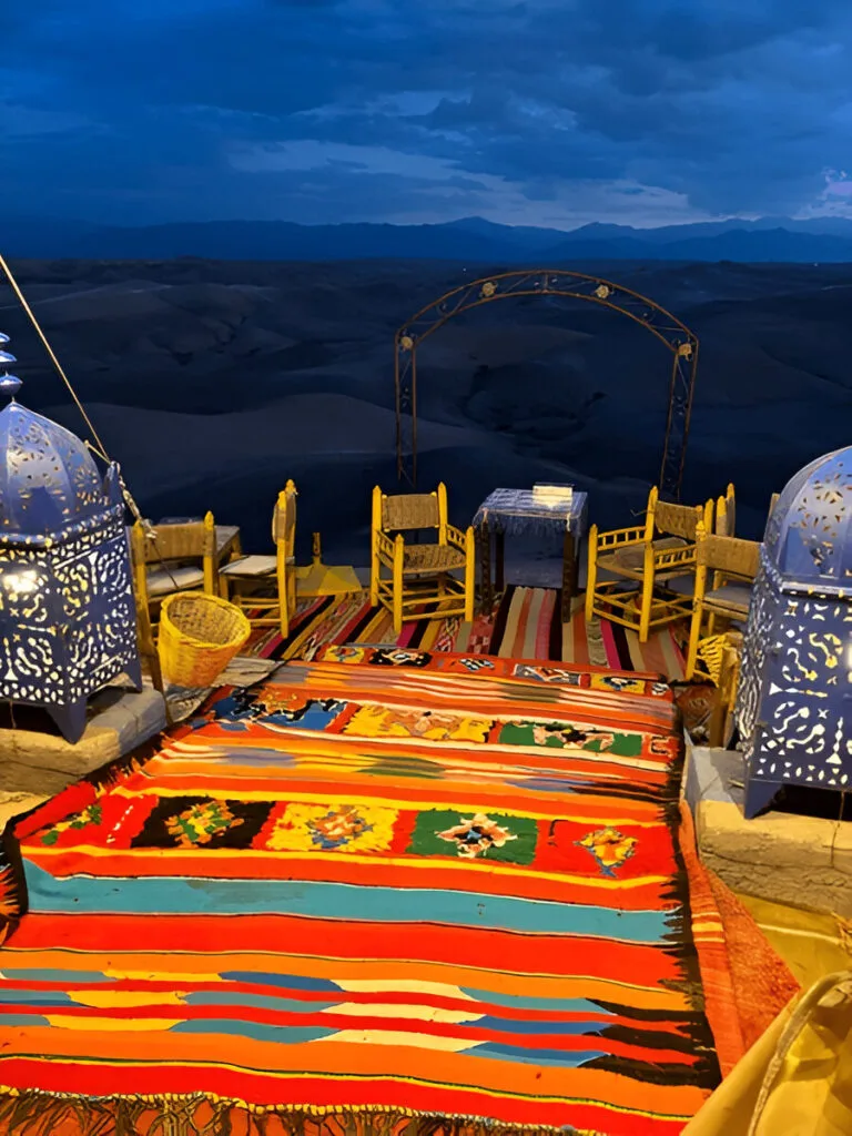 Dinner table laid out at a camp in the Agafay desert at dusk, with the High Atlas behind