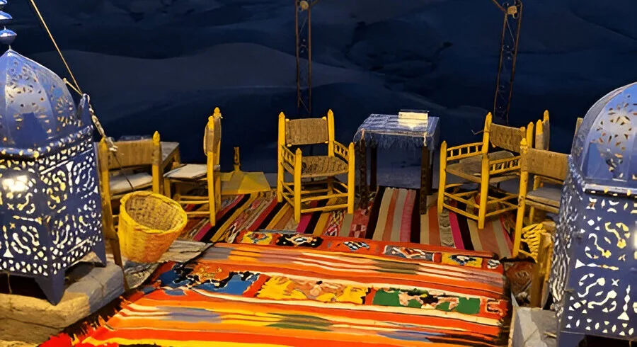 Dinner table laid out at a camp in the Agafay desert at dusk, with the High Atlas behind